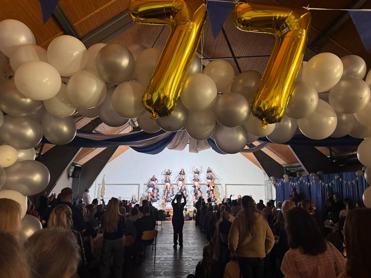 Die Blauen Jungs auf der Bühne des Kasinos; über dem Publikum hängen goldene 77-Ballons